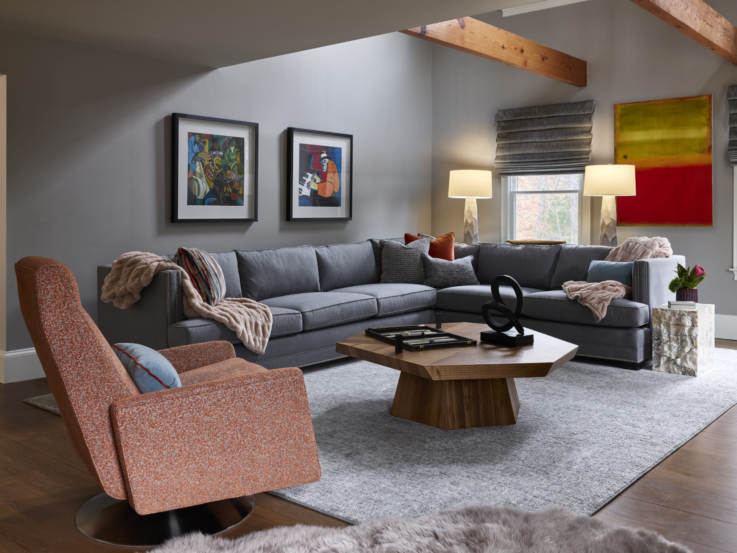 Modern living room with a gray sectional sofa, orange armchair, wooden coffee table, and abstract wall art—an inviting example of luxury interior design by an acclaimed interior designer in Massachusetts.