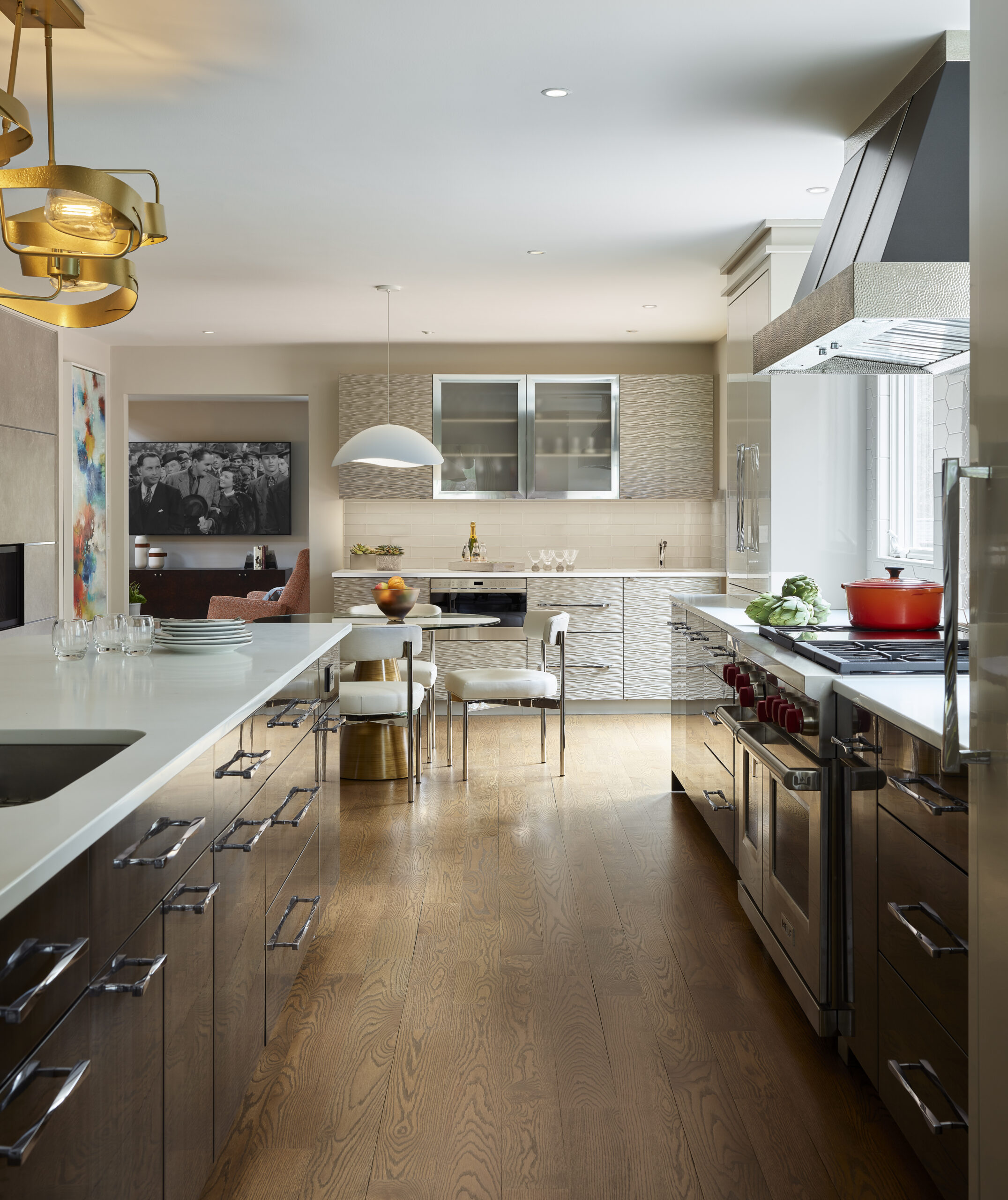 Modern kitchen with white countertops, stainless steel appliances, wood cabinets, and a dining area in the background featuring pendant lighting and contemporary decor—a stunning example of luxury interior design by an expert interior designer in Massachusetts.