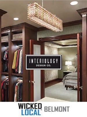 A modern walk-in closet leads to a bedroom with a bed, side table, and lamp; logos for Interiology Design Co. and Wicked Local Belmont highlight this showcase of luxury interior design by an expert interior designer in Massachusetts.