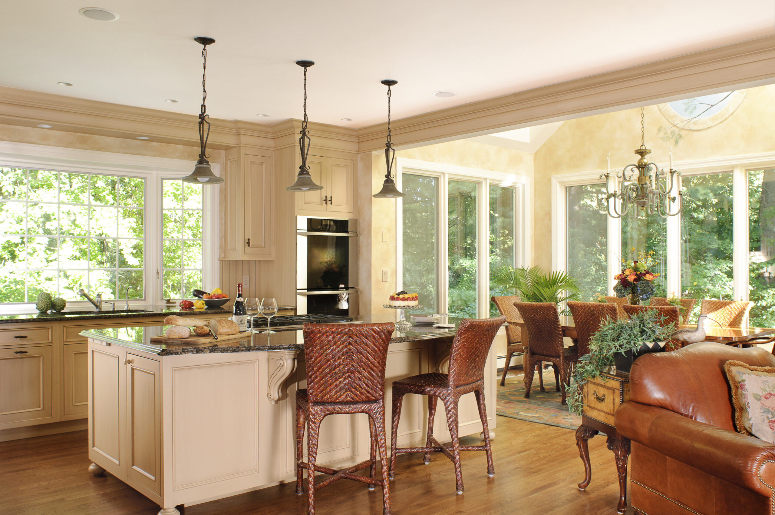Spacious kitchen with cream cabinets, a large island, woven bar stools, and an adjoining dining area filled with natural light—expertly crafted by an Interior Designer Massachusetts for true luxury interior design.