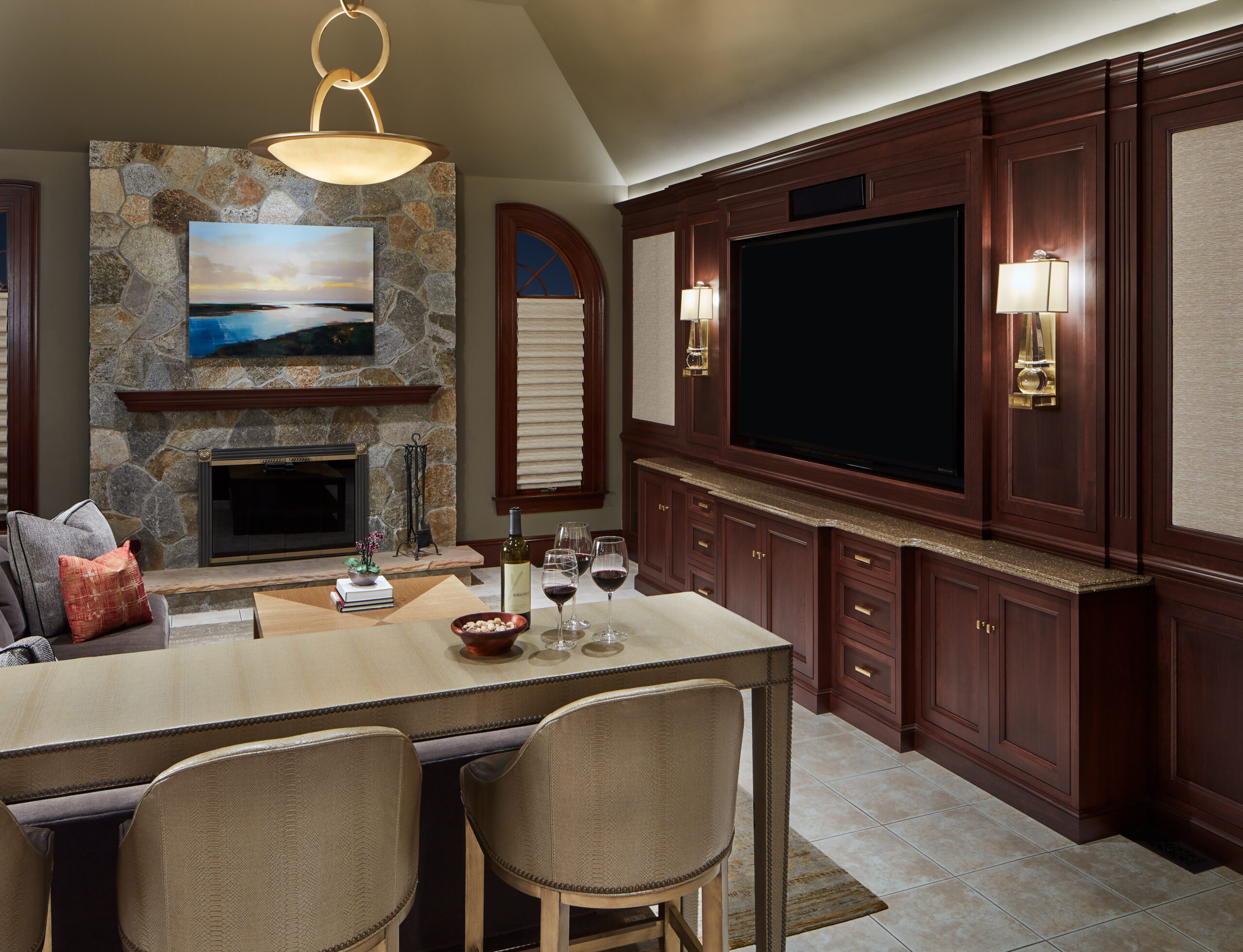 A living room with a stone fireplace, wall-mounted TV, wooden cabinets, and a chic dining area—perfectly capturing luxury interior design by an expert interior designer in Massachusetts. Wine glasses and snacks await on the table.