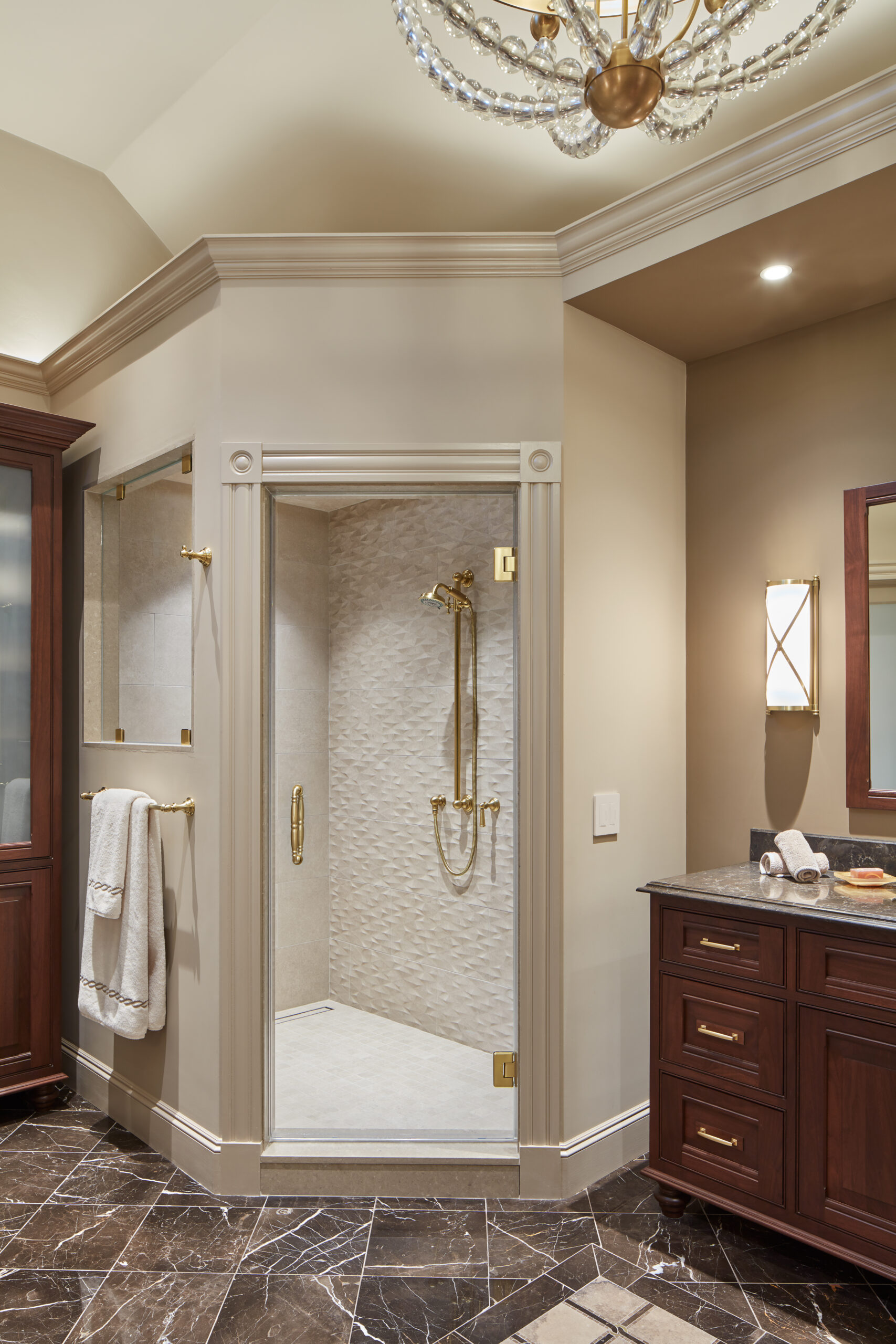 A modern bathroom by an Interior Designer in Massachusetts, featuring a glass-enclosed shower, gold fixtures, dark wood cabinets, marble floor, and a decorative ceiling light—epitomizing luxury interior design.