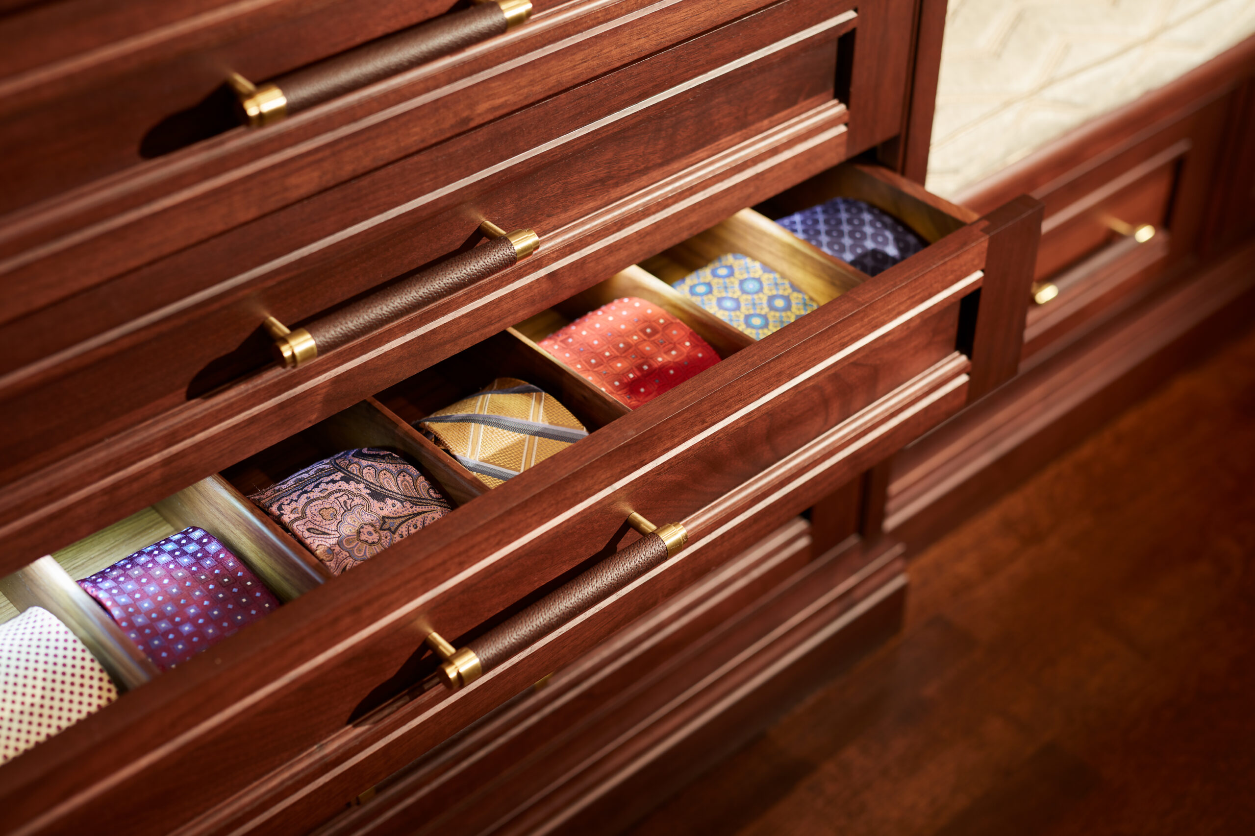 A wooden drawer is open to reveal neatly organized ties in various colors and patterns, each separated by individual compartments—a perfect touch for luxury interior design enthusiasts.