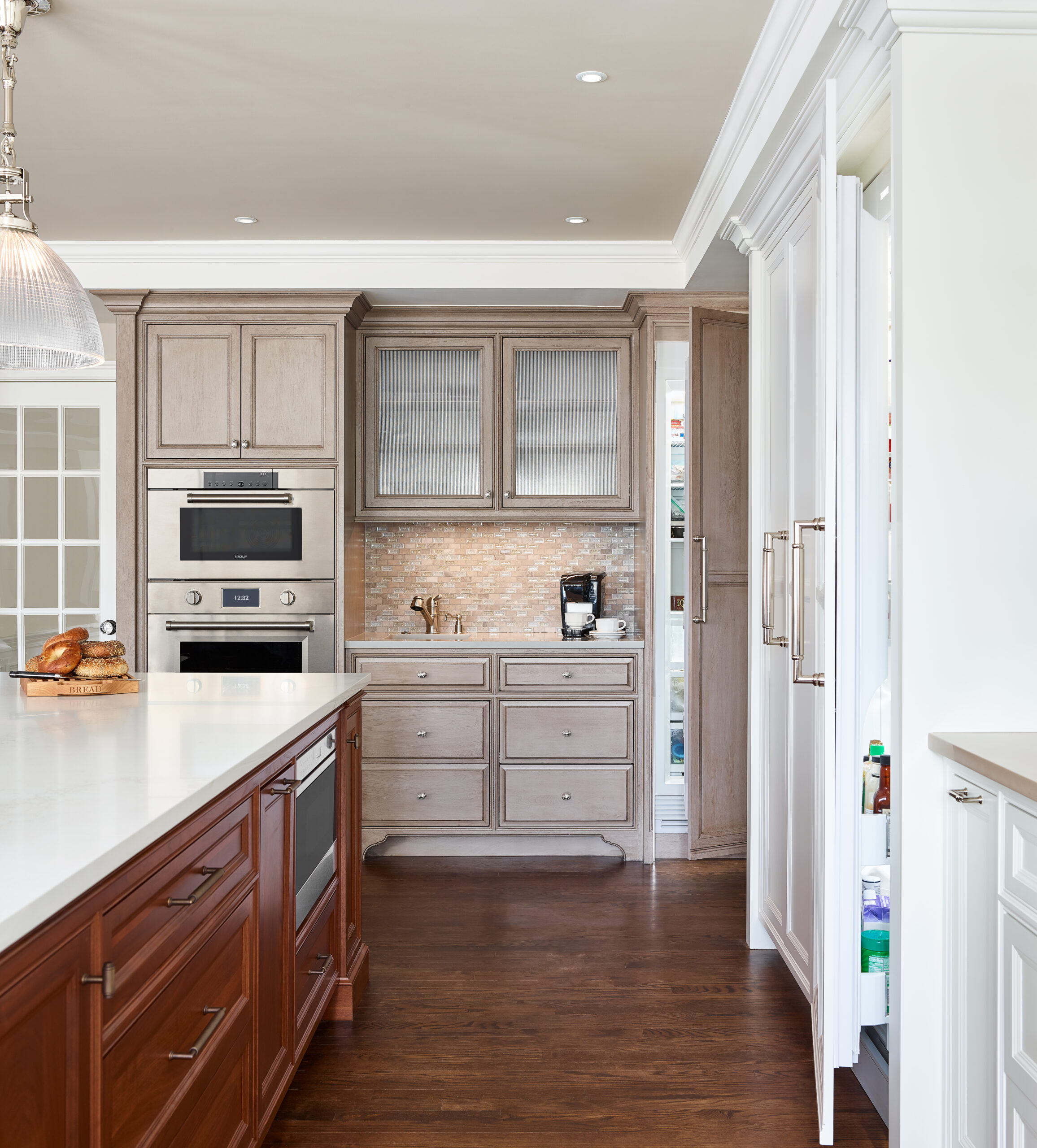Modern kitchen with light wood cabinets, built-in oven and microwave, marble island with cooktop, and an open refrigerator—an ideal showcase of luxury interior design by a talented interior designer in Massachusetts.