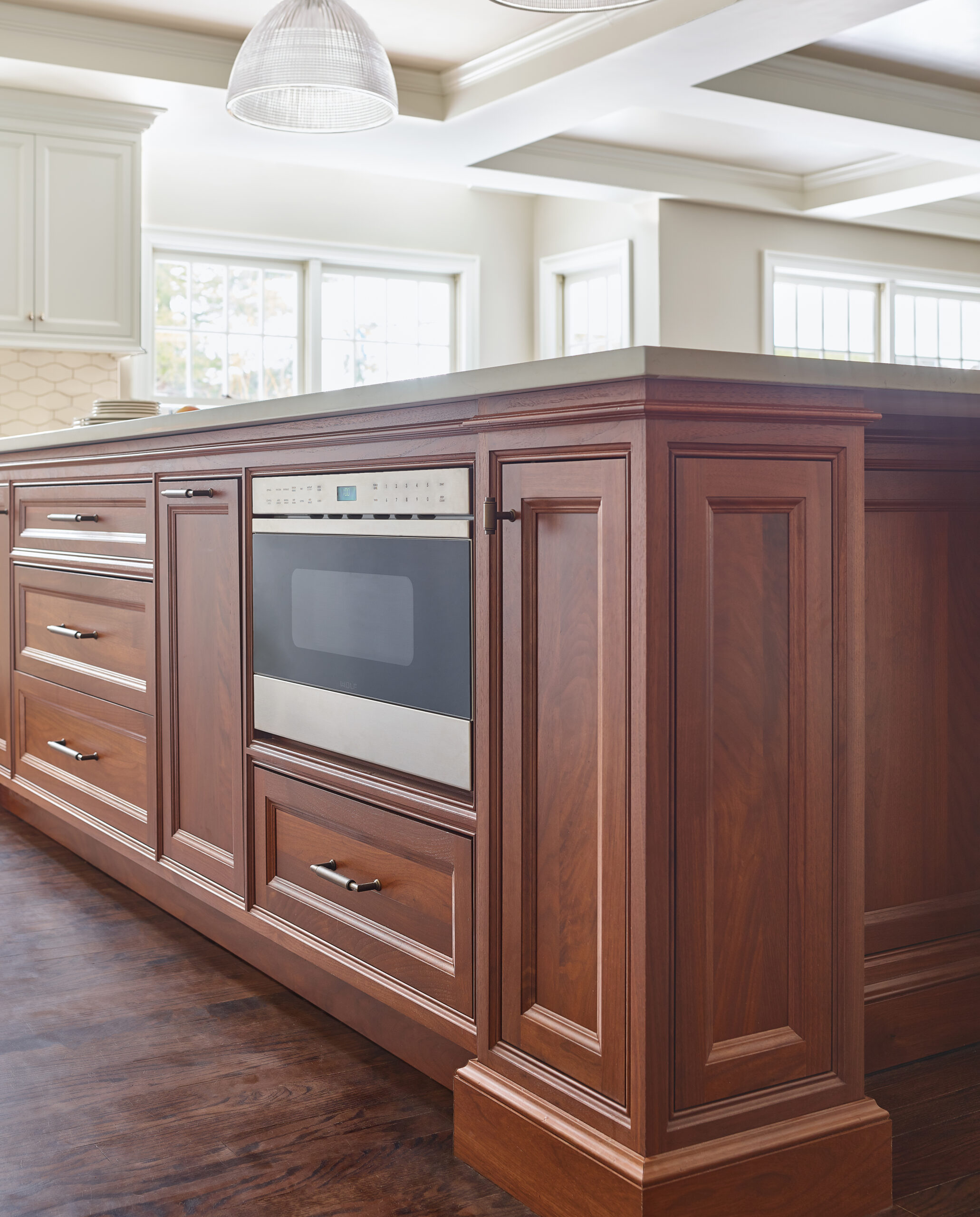 A built-in microwave is installed in a wooden kitchen island with paneled cabinets and drawers, set on a dark hardwood floor—showcasing the elegance of luxury interior design.