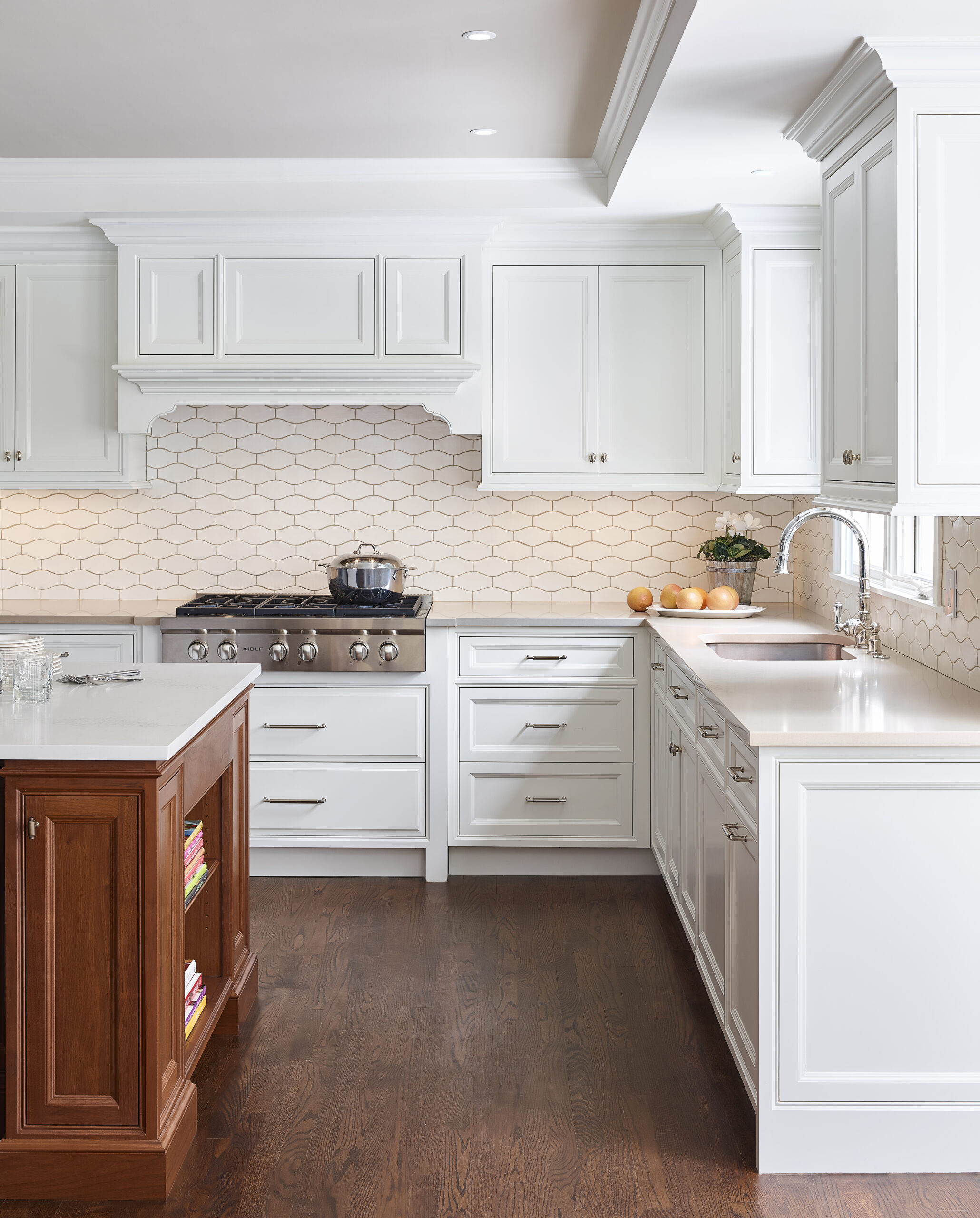 Modern kitchen with white cabinets, hexagonal tile backsplash, stainless steel stove, and a wooden island with open shelves—an example of luxury interior design by a top interior designer in Massachusetts.