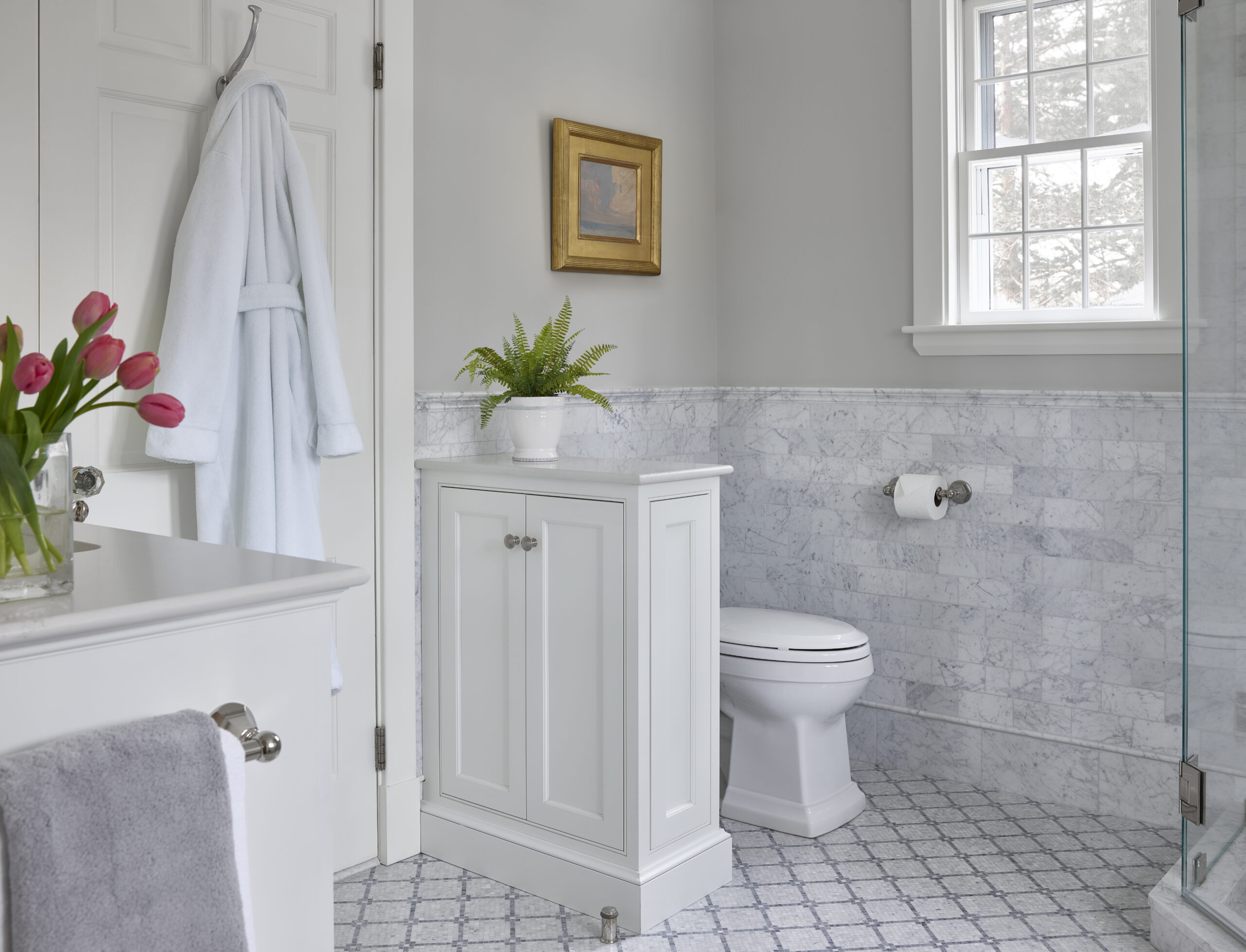 A bright bathroom with a white cabinet, marble tile walls, and elegant details like a bouquet of tulips showcases the touch of an Interior Designer Massachusetts, blending luxury interior design with comfort and style.