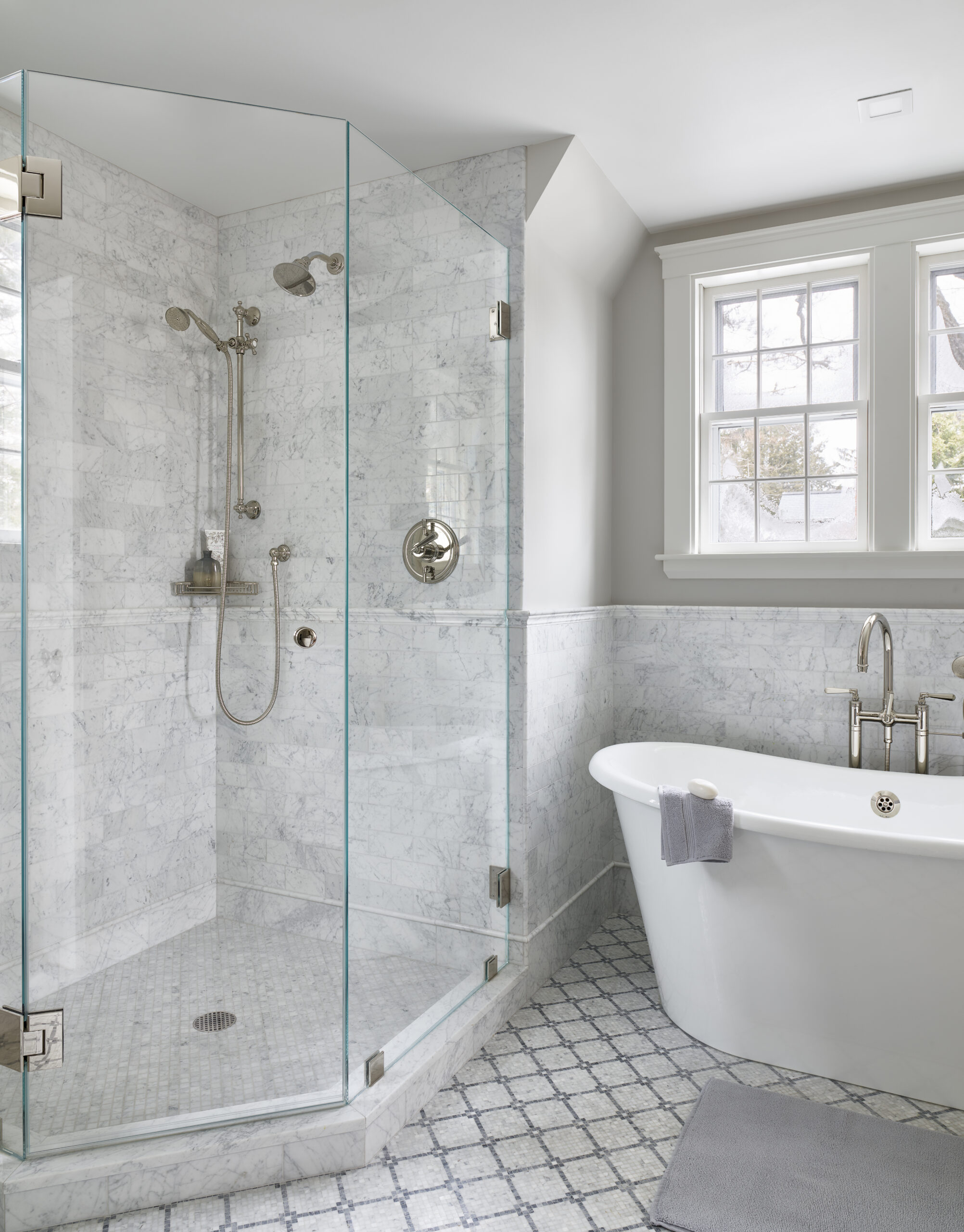 Modern bathroom with a glass-enclosed corner shower, wall-mounted fixtures, a freestanding bathtub draped with a towel, and white marble surfaces—perfect for those seeking luxury interior design by an expert interior designer in Massachusetts.