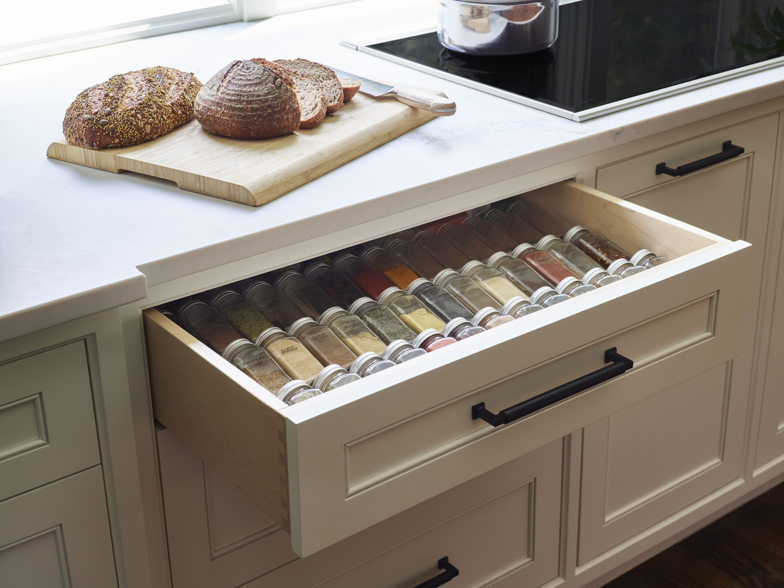 An open kitchen drawer with neatly organized spice jars, next to a cutting board with two loaves of bread, one partially sliced—showcasing the elegance of luxury interior design.