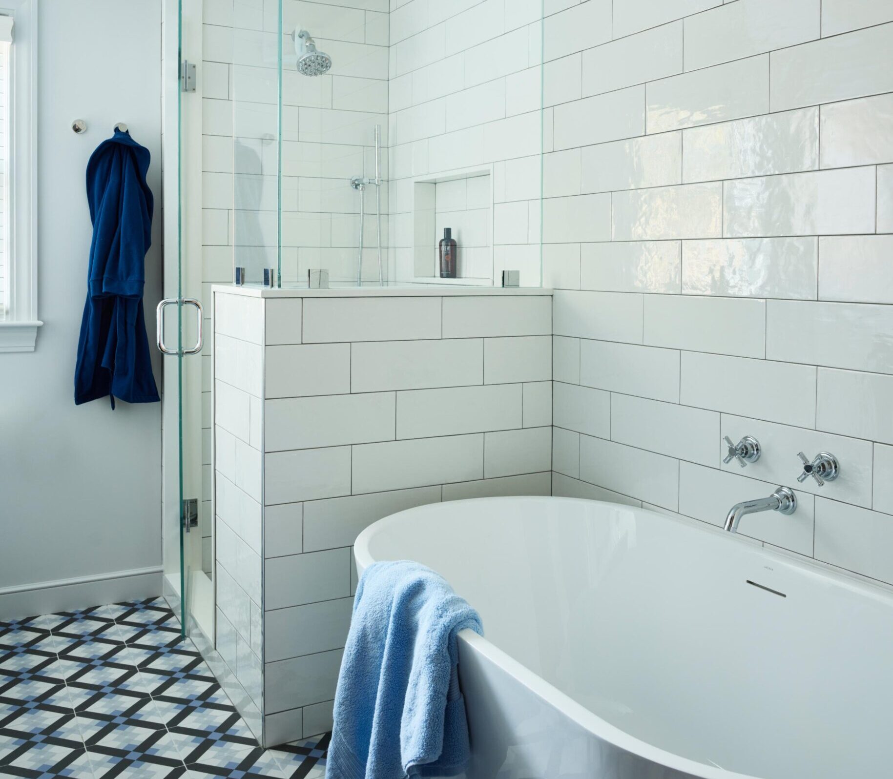 Modern bathroom interior design featuring white subway tile walls, a glass-enclosed shower, freestanding bathtub with a blue towel, and a patterned tile floor.