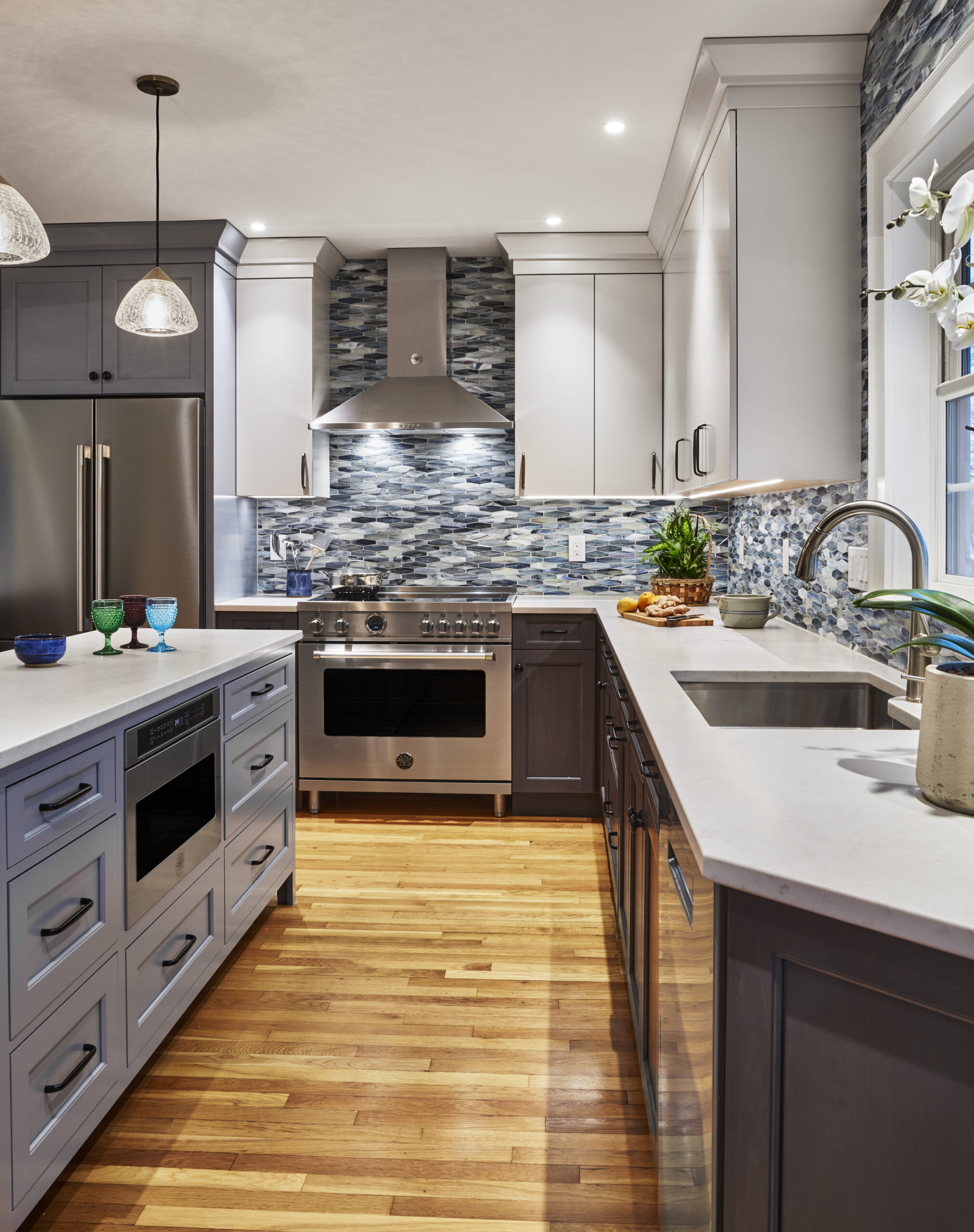 Modern kitchen with stainless steel appliances, gray cabinets, an island with drawers, a tile backsplash, and wooden floors—perfectly showcasing Luxury Interior Design by a top Interior Designer Massachusetts.