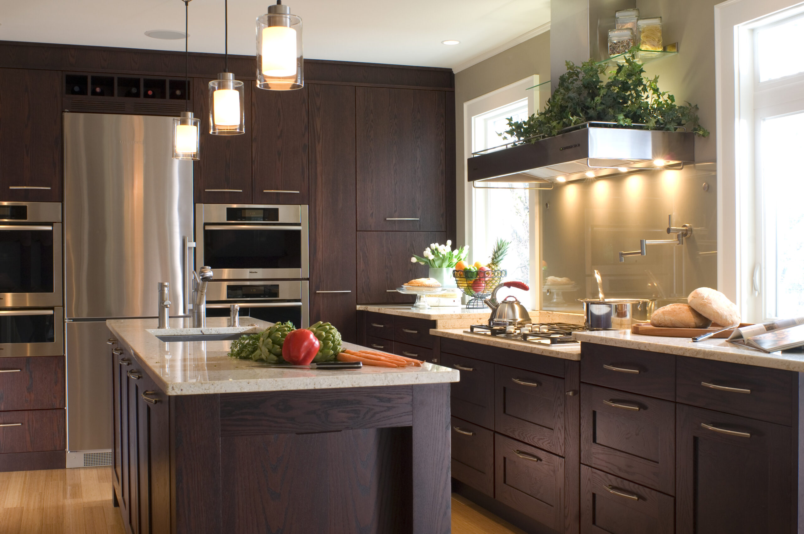 Modern kitchen with dark wood cabinets, stainless steel appliances, kitchen island with vegetables, and under-cabinet lighting. Crafted by a top Interior Designer Massachusetts, this space showcases luxury interior design details throughout.