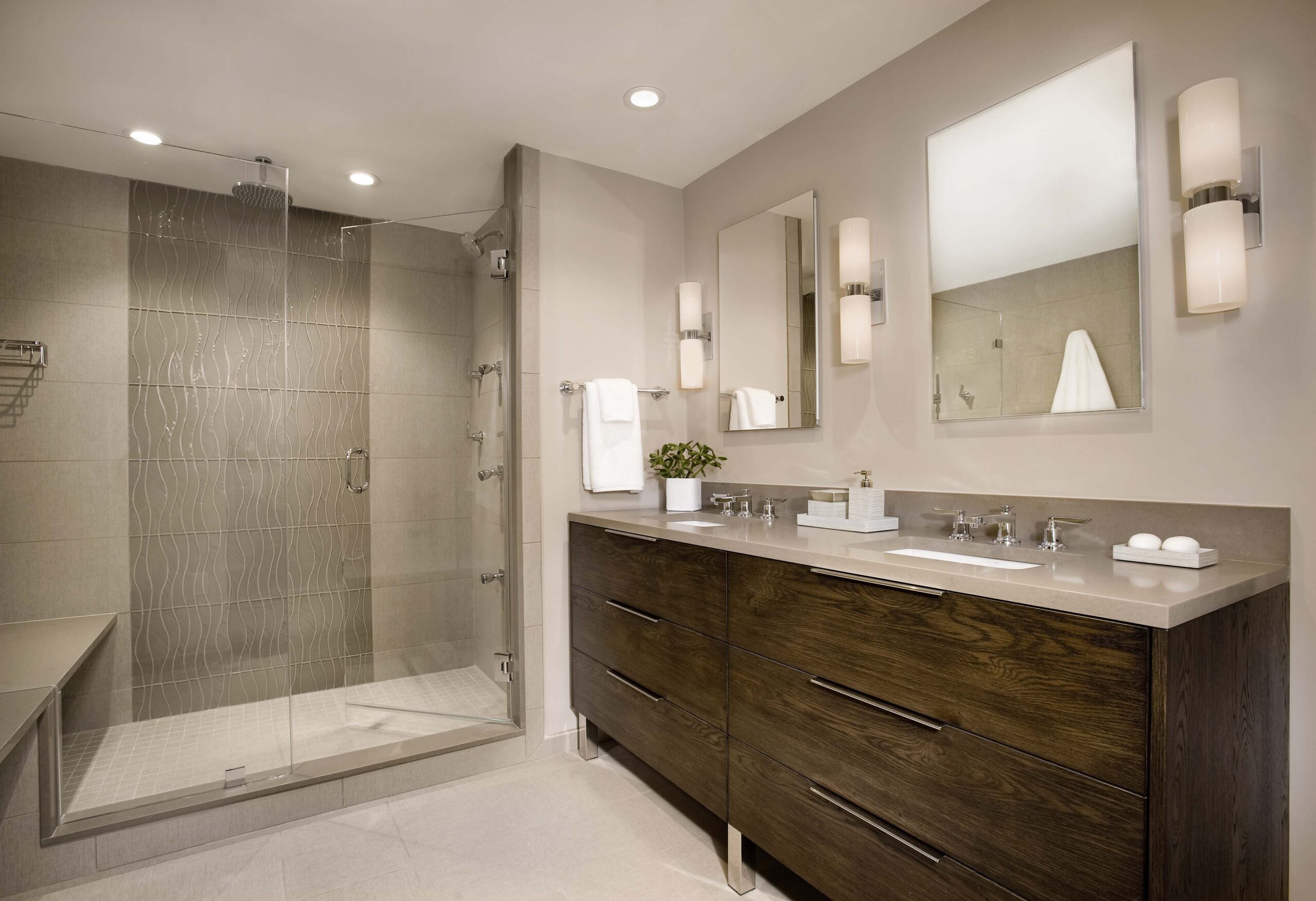 Modern bathroom with a large glass-enclosed shower, luxury interior design touches, double vanity with dark wood cabinets, wall-mounted sinks, and neutral-toned walls and flooring.