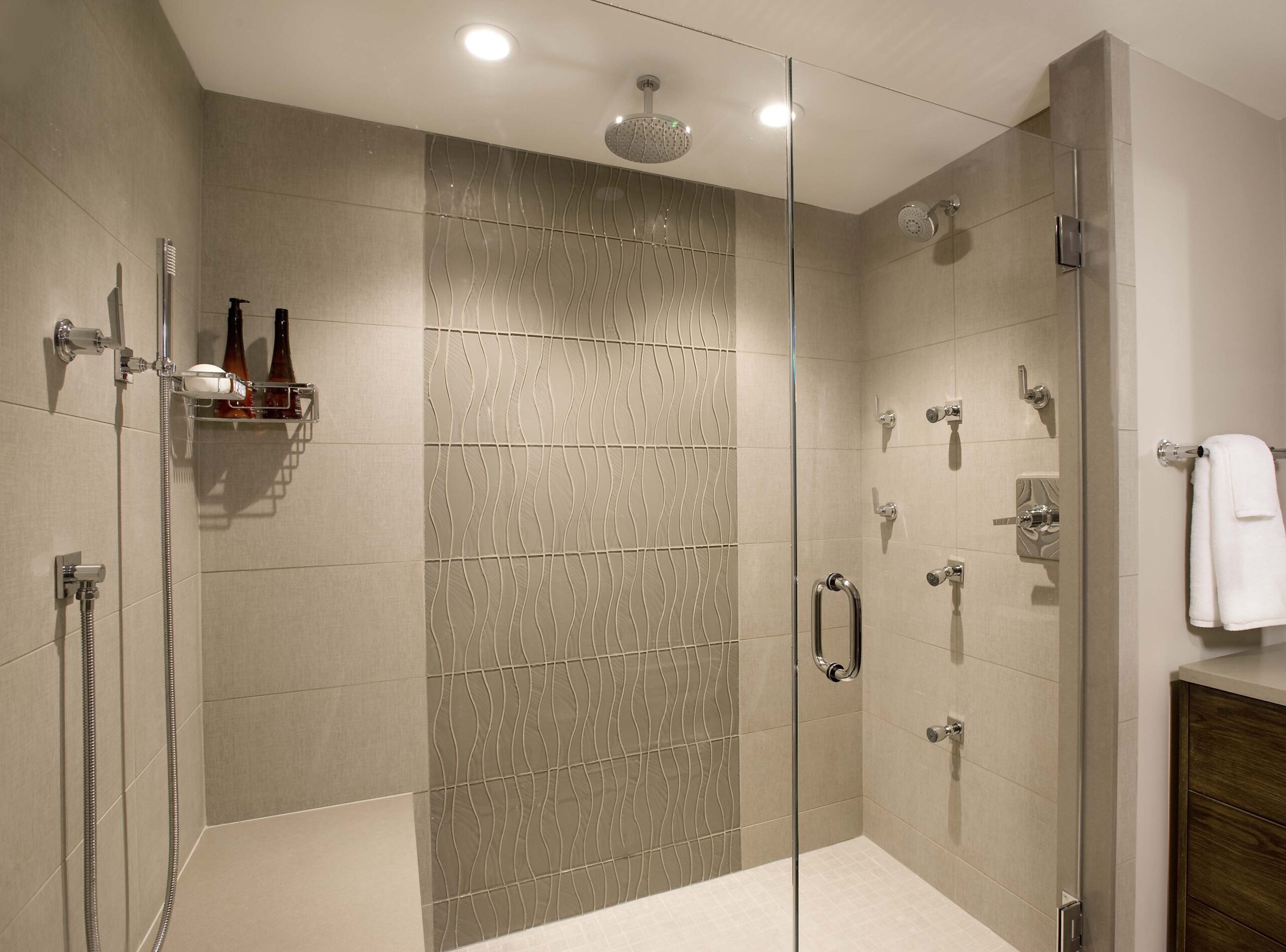 Spacious walk-in shower with beige tiles, a glass door, overhead rain shower, multiple wall jets, towel on rack, and a built-in bench—perfect for those who appreciate luxury interior design.