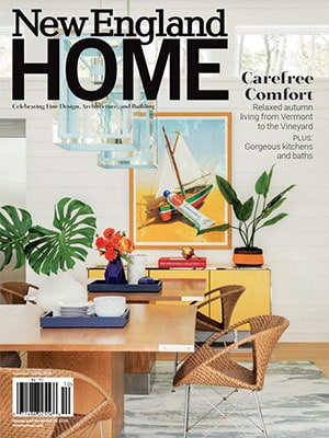 Cover of New England Home magazine featuring a modern dining room with wicker chairs, a wooden table, vibrant flowers, and colorful artwork—highlighting luxury interior design by an acclaimed interior designer in Massachusetts.