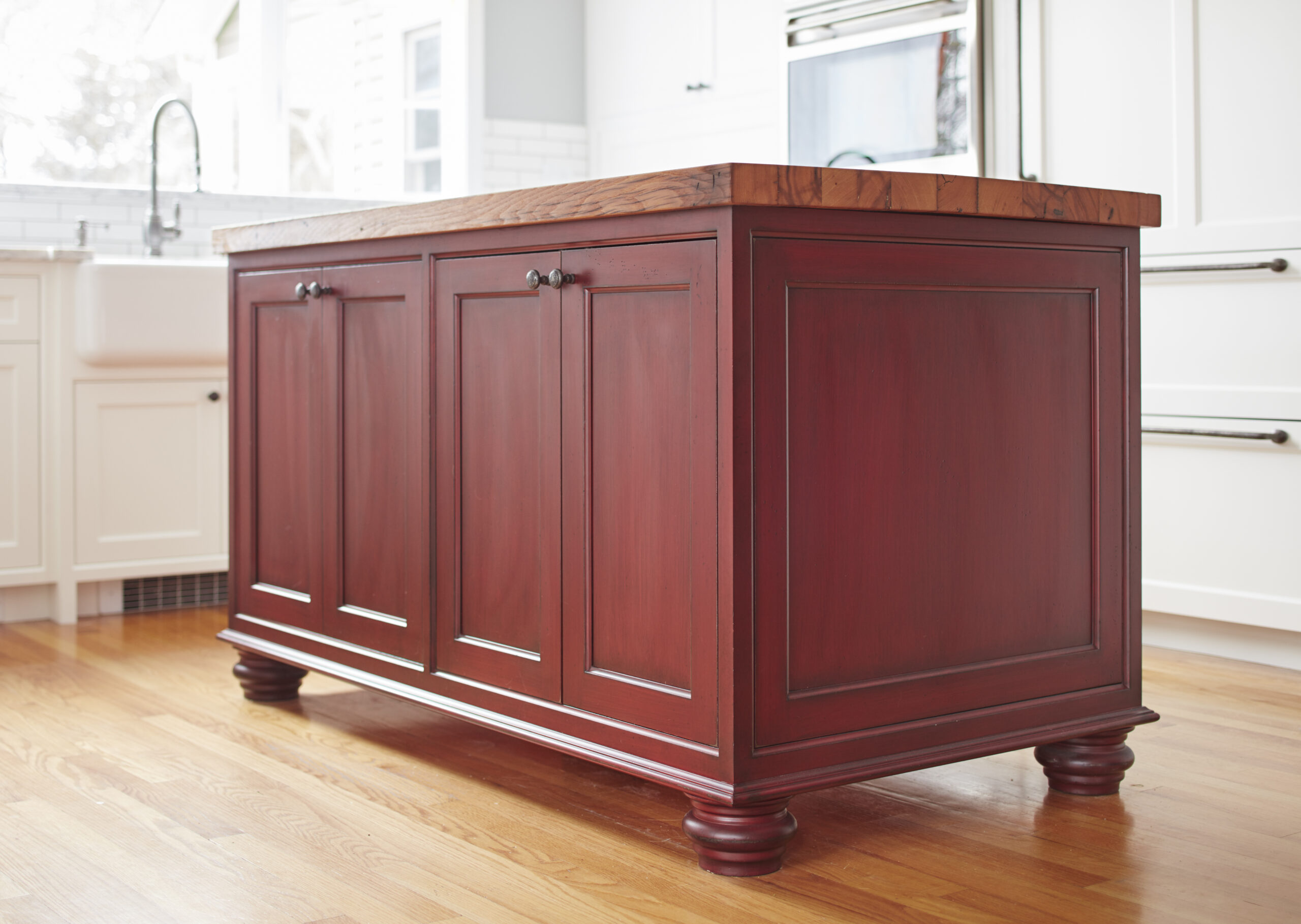 A red wooden kitchen island with a butcher block countertop and paneled doors, set on a light wood floor in a bright kitchen—perfect inspiration for luxury interior design by an interior designer in Massachusetts.