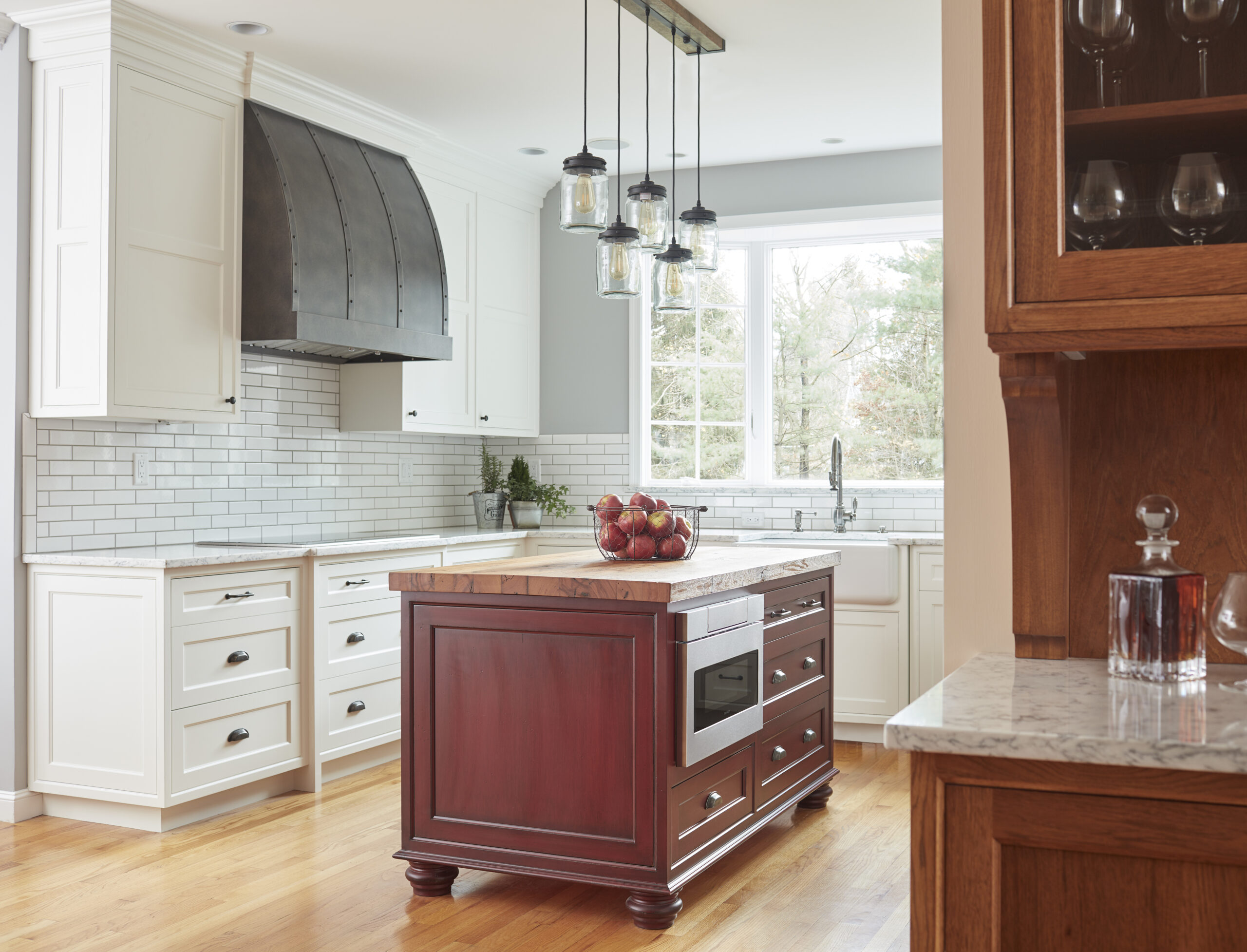 A modern kitchen with white cabinets, stainless steel range hood, subway tile backsplash, and a wooden island with a microwave. Designed with luxury interior design elements under pendant lights for a sophisticated touch.