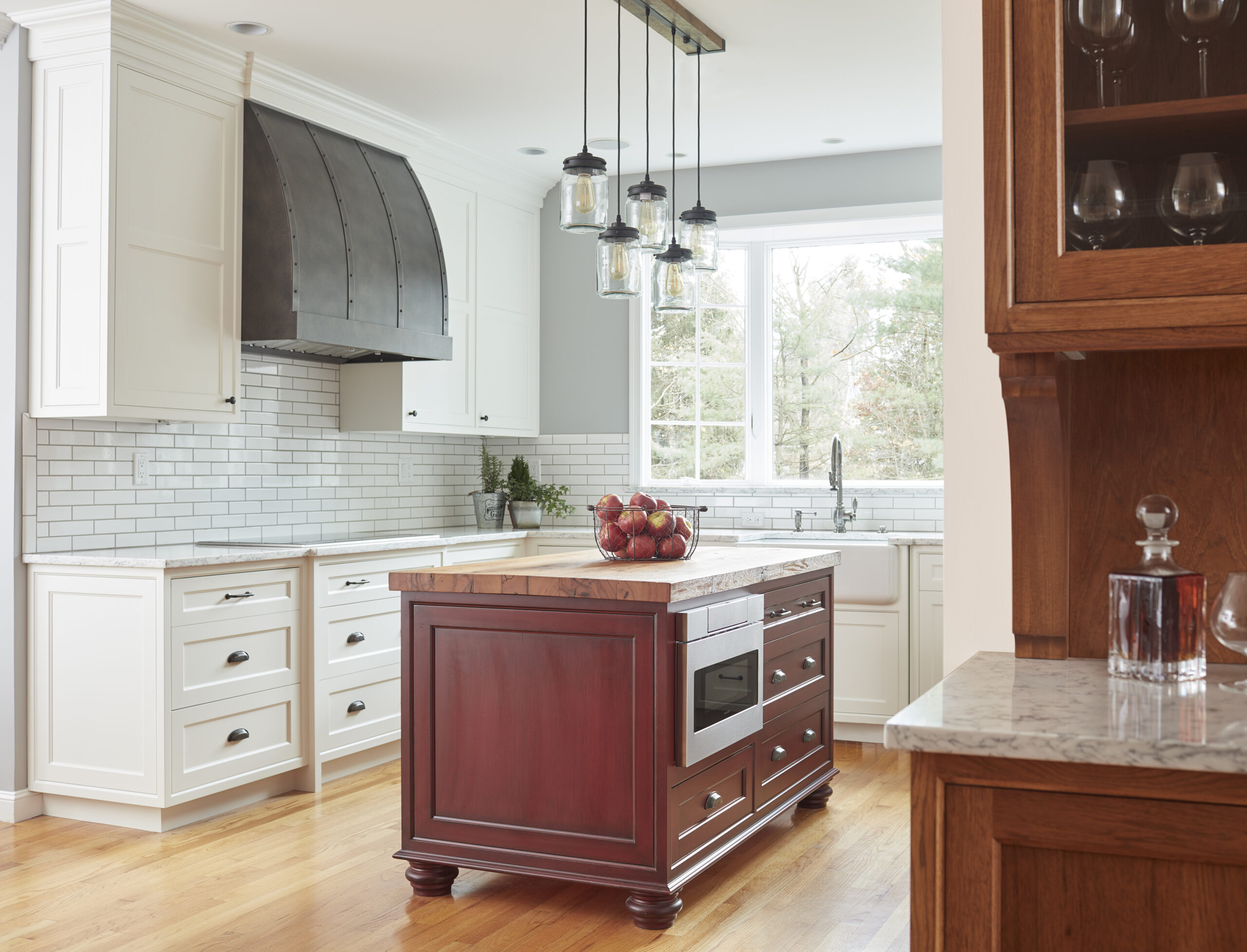Modern kitchen with white cabinets, subway tile backsplash, wood island with built-in microwave, pendant lights, and a bowl of apples. Designed by an Interior Designer in Massachusetts, this space exudes luxury interior design and abundant natural light.