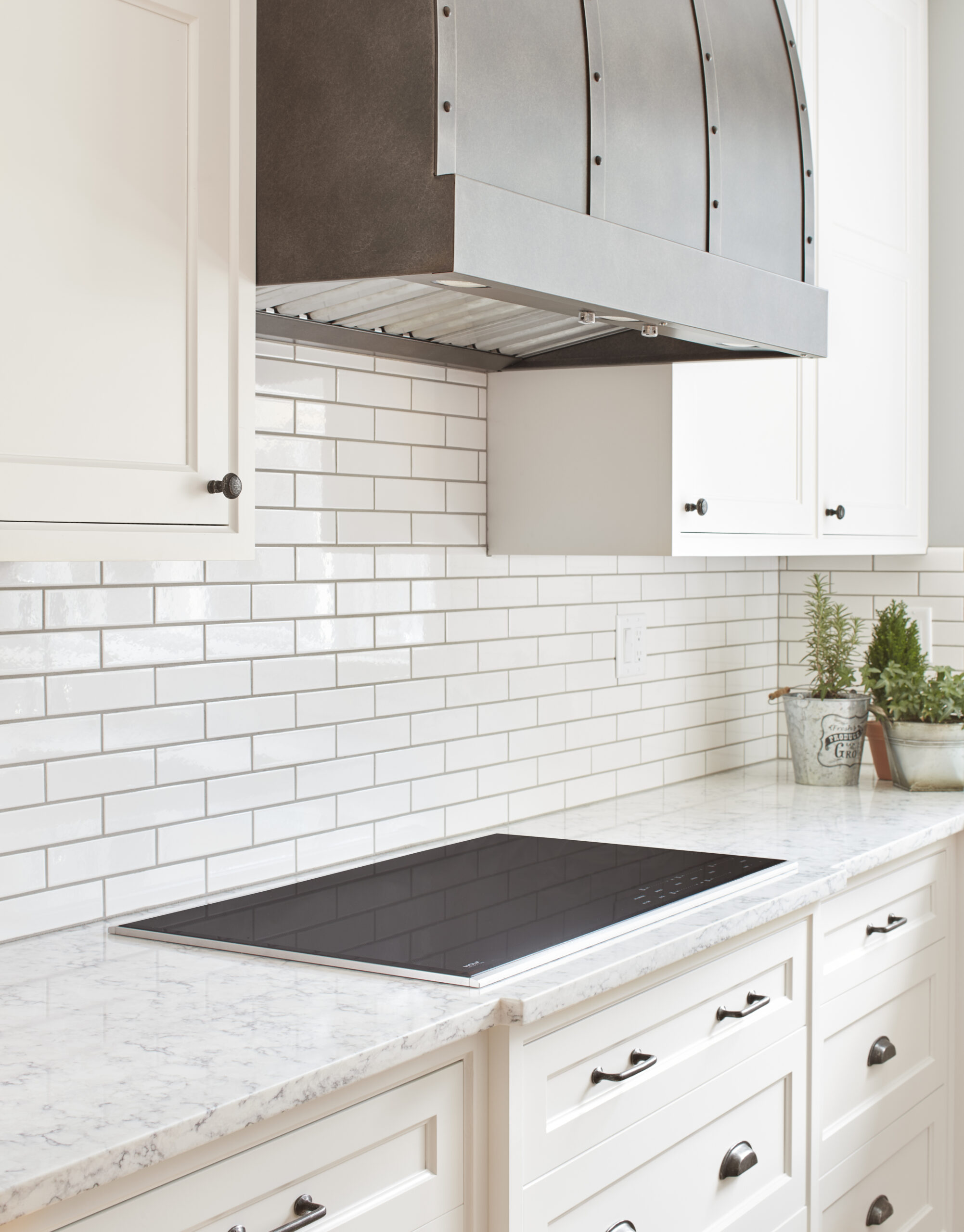 Modern kitchen with a marble countertop, electric cooktop, white cabinet drawers, subway tile backsplash, and a large stainless steel range hood—showcasing thoughtful Luxury Interior Design by top Interior Designer Massachusetts.