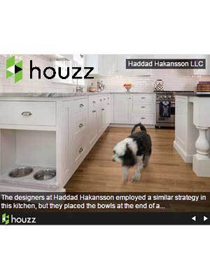 A black and white dog walks in a modern white kitchen with built-in pet bowls in a lower cabinet, showcasing Luxury Interior Design. Houzz and Haddad Hakansson LLC logos are visible.