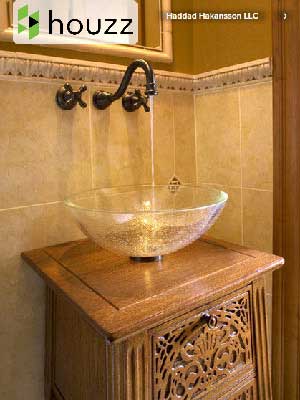 Glass vessel sink with running water on a wooden vanity featuring decorative carving, set against a tiled bathroom wall. Showcasing Luxury Interior Design by Houzz and Haddad Hakansson LLC, premier Interior Designer Massachusetts.