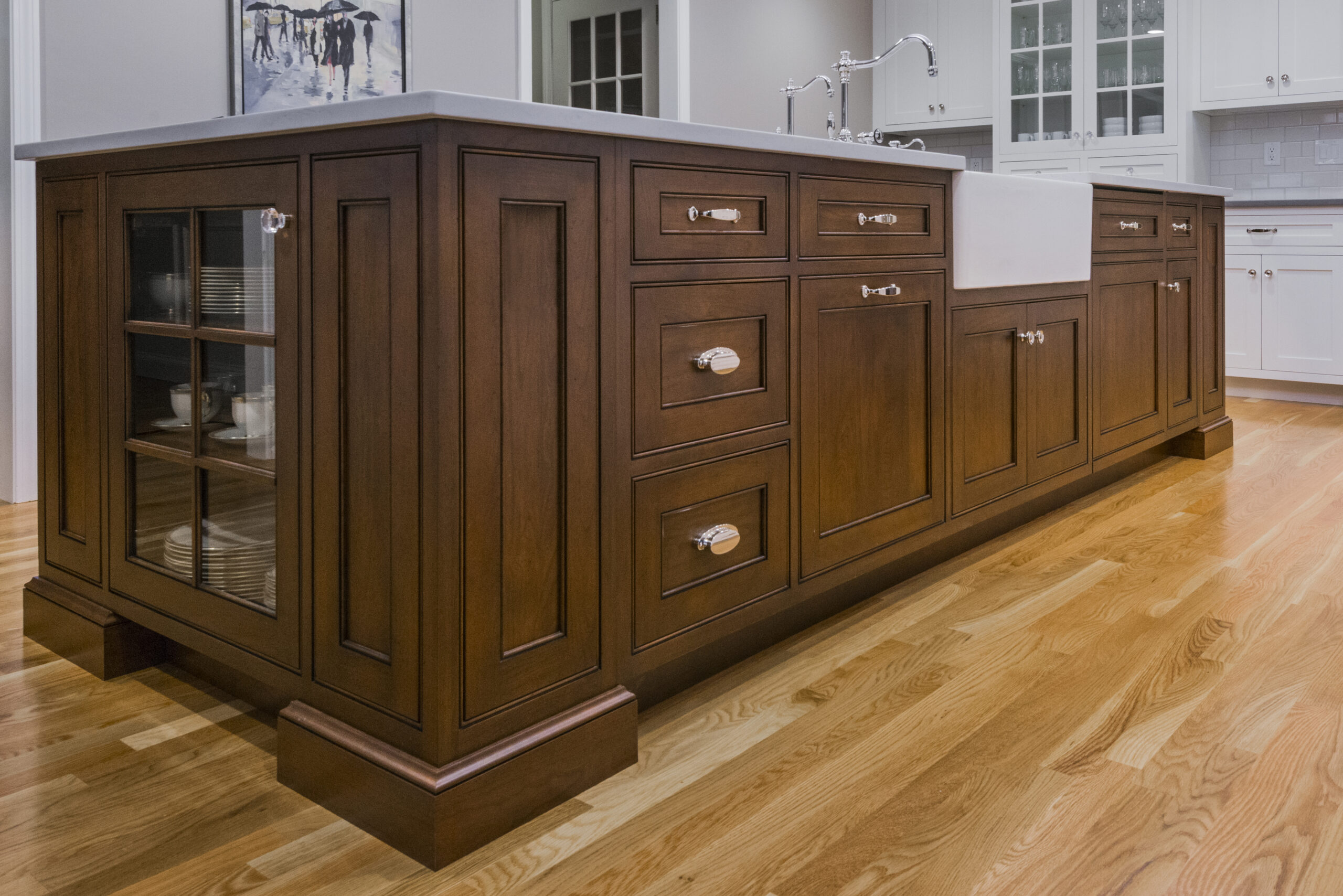 Large wooden kitchen island with a white countertop, farmhouse sink, drawers, and cabinets, set on a polished hardwood floor in a bright kitchen—perfect for those seeking luxury interior design.
