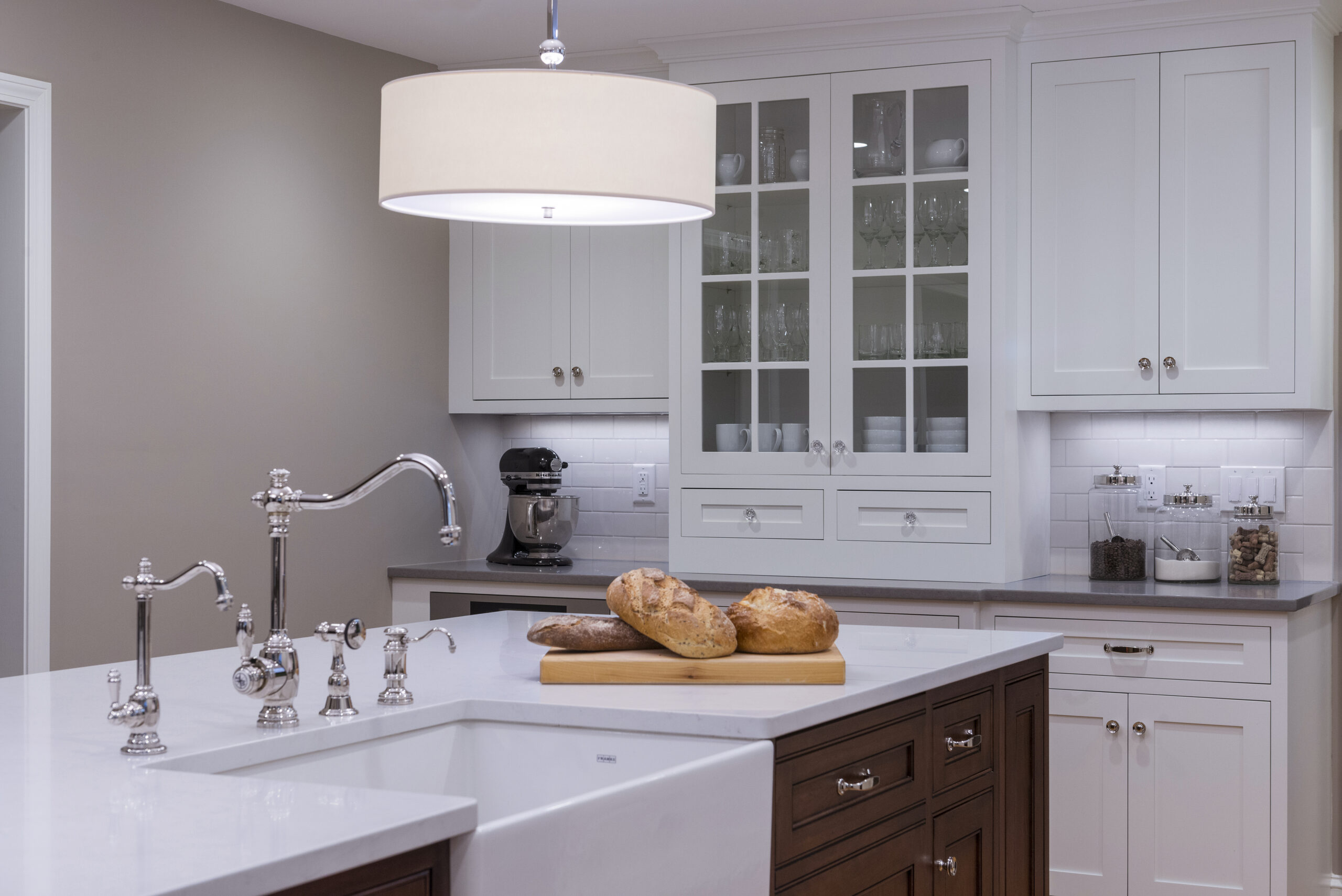 Modern kitchen with white cabinets, a large island with a sink, chrome fixtures, and three loaves of bread on a wooden cutting board—a perfect example of luxury interior design by an expert interior designer in Massachusetts.