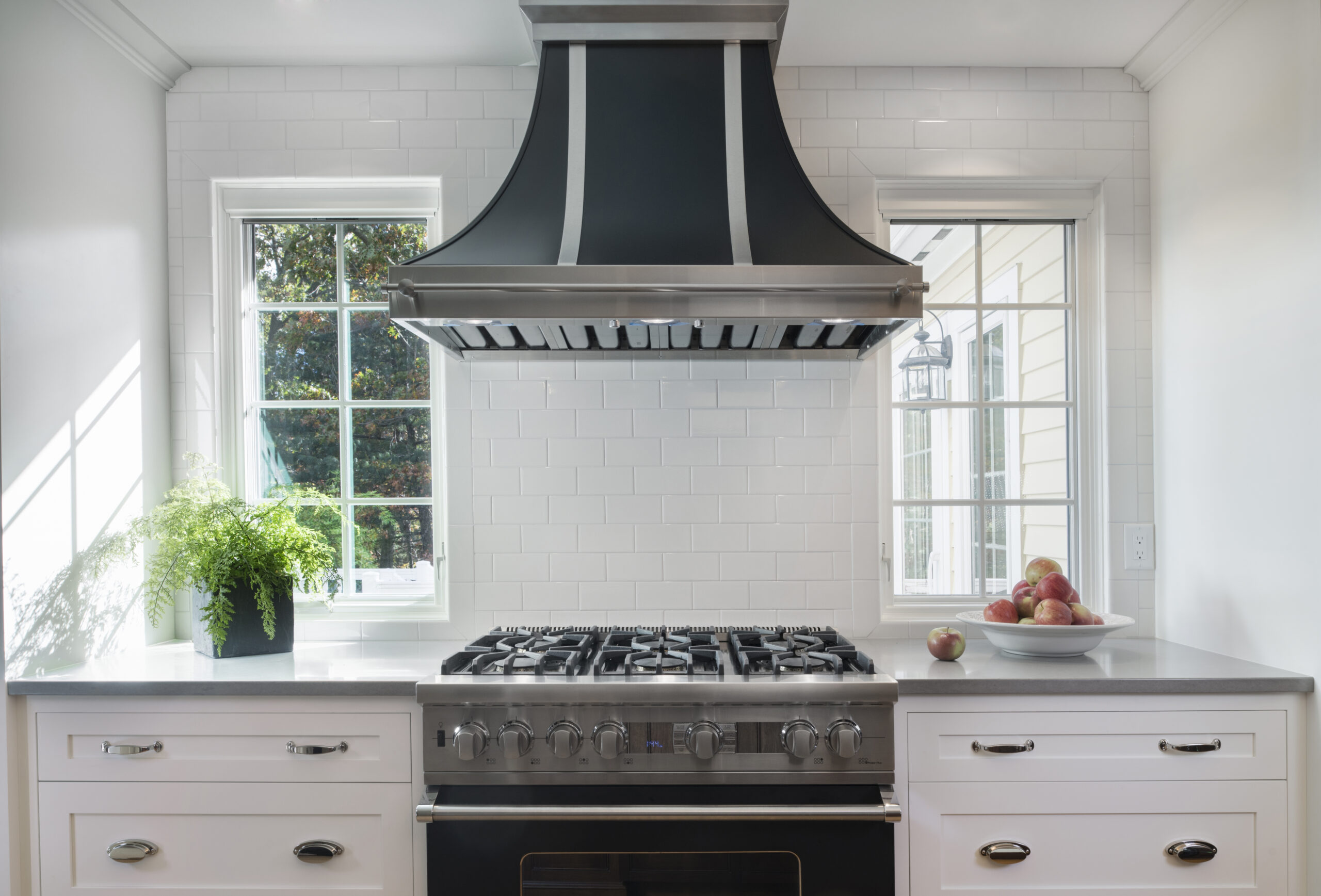 Modern kitchen featuring a stainless steel gas stove, large black range hood, white tile backsplash, and natural light—an inviting space showcasing Luxury Interior Design expertise.