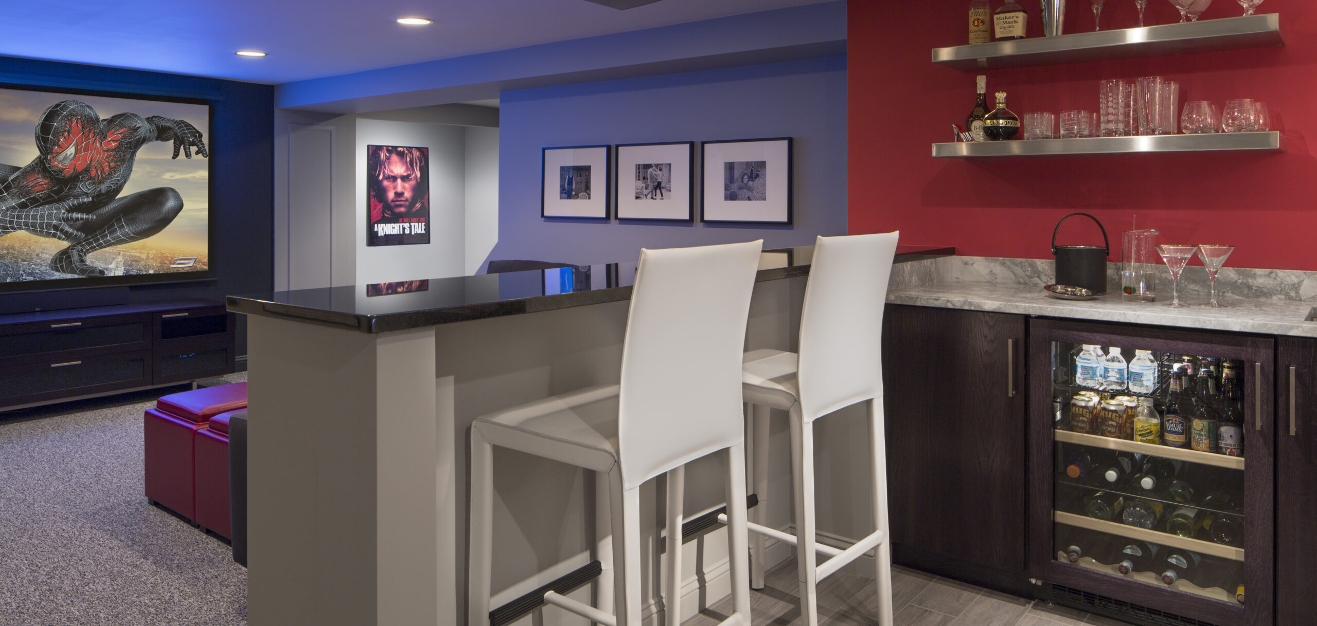 A modern home bar area with two white barstools, a glassware shelf, a mini fridge, and movie posters on the wall—perfectly curated for stylish entertaining by an Interior Designer Massachusetts expert in luxury interior design.