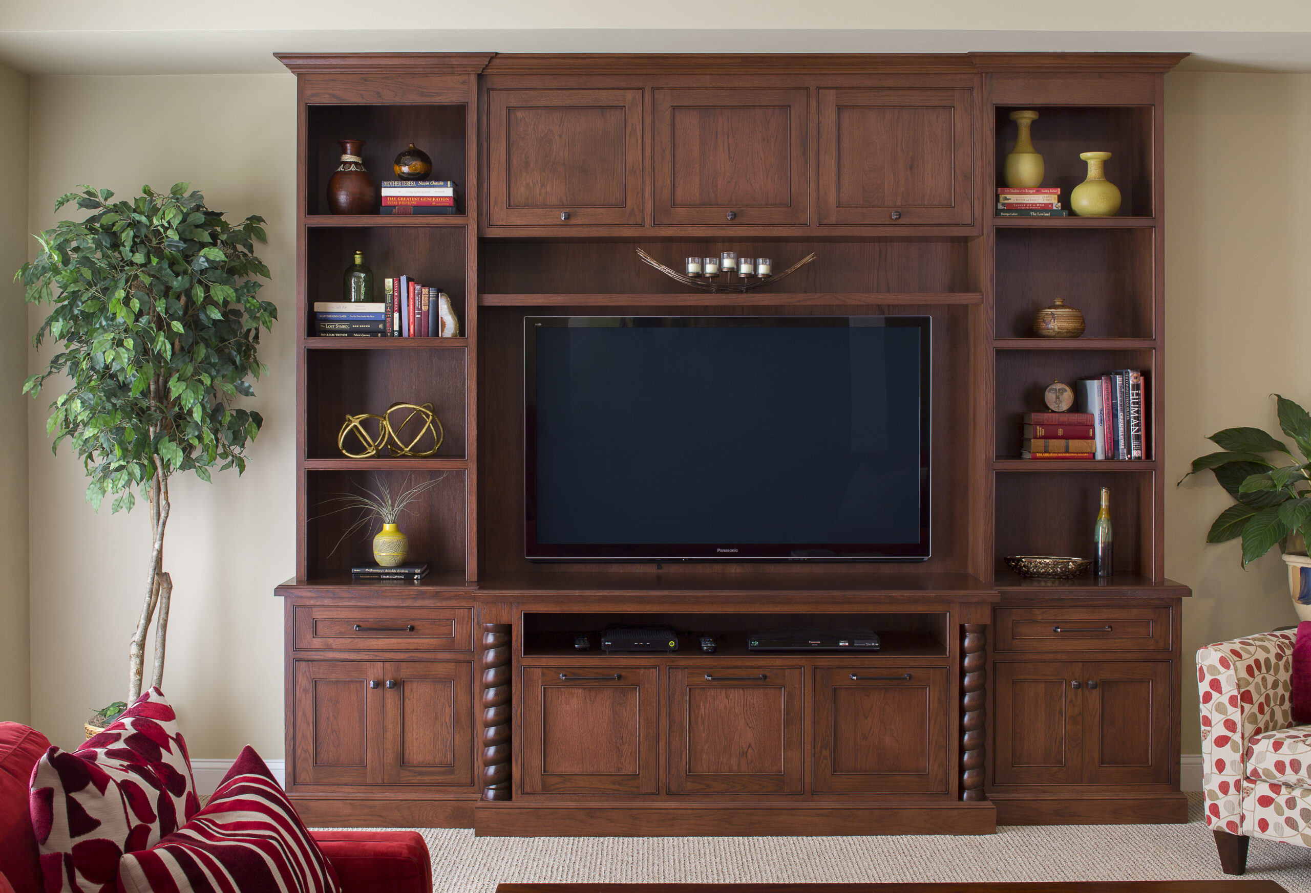 A large wooden entertainment center with shelves, cabinets, and a flat-screen TV, decorated with books, vases, and ornaments. A green potted plant is on the left—perfect for a touch of luxury interior design in any home.
