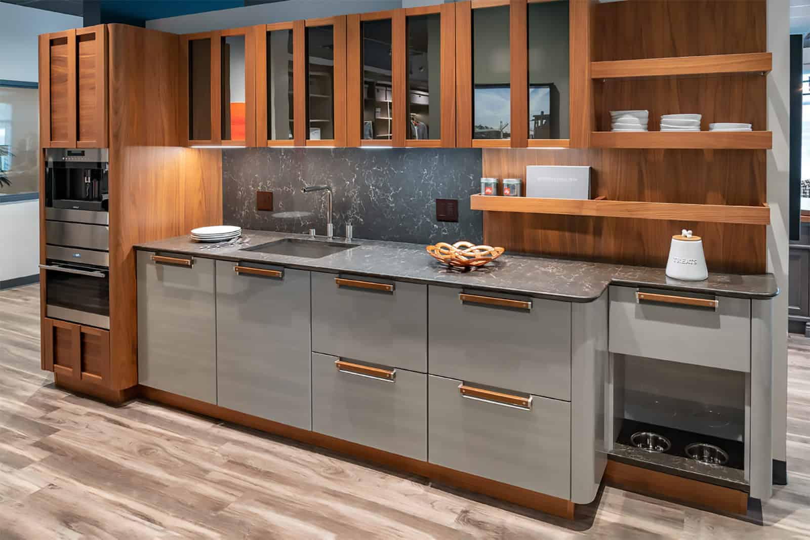 Modern kitchen featuring wood and gray cabinets, marble countertop, built-in appliances, open shelving with dishes, and a built-in pet feeding station on a wood floor—perfect for those who appreciate luxury interior design.