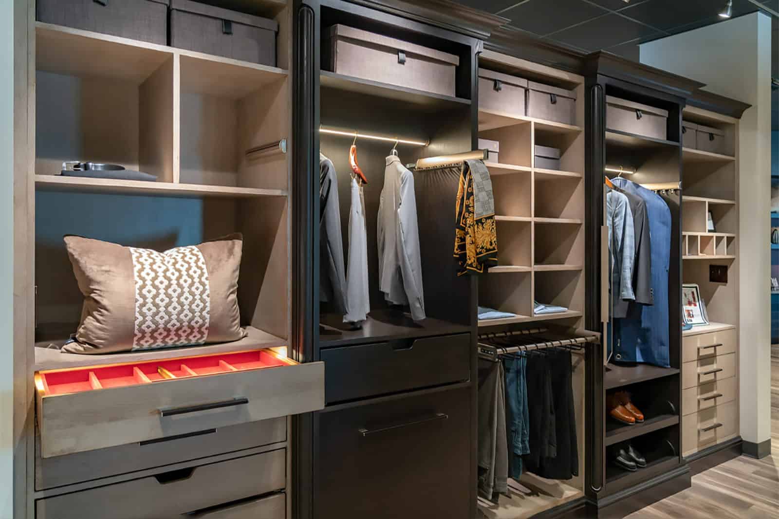Modern walk-in closet with open shelves, hanging clothes, drawers, a pillow in a display drawer, and organized storage compartments—an example of Luxury Interior Design by an expert Interior Designer Massachusetts.