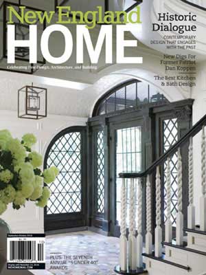 Cover of New England Home magazine featuring a bright entryway curated by a top Interior Designer Massachusetts, with dark-framed double doors, a staircase with white spindles, and a large vase of flowers on a table.