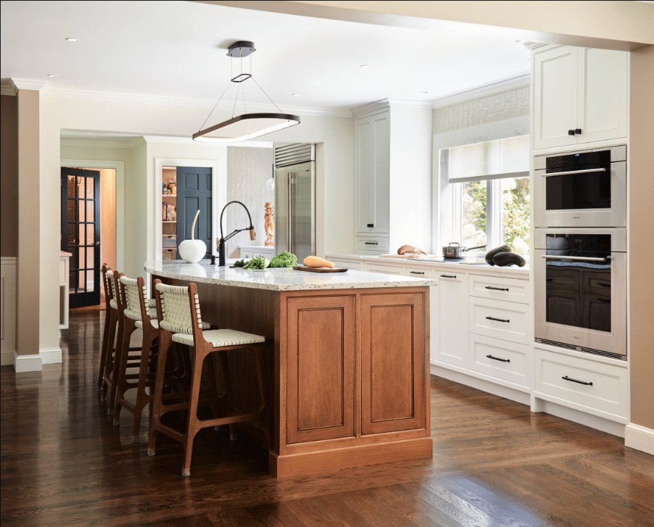 Modern kitchen with a wooden island, four chairs, white cabinets, built-in ovens, large fridge, countertop appliances, and a window above the sink.